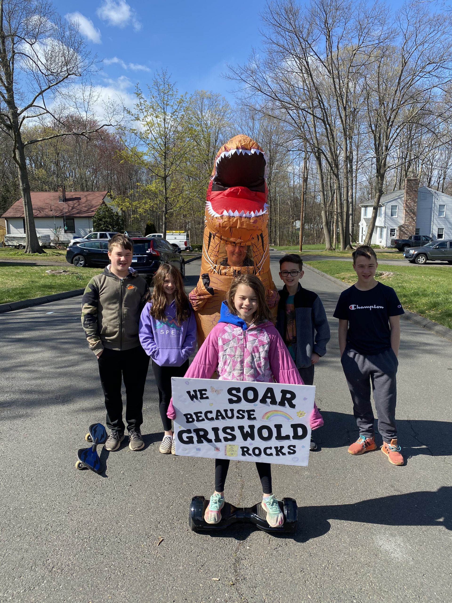 Five children and an inflatable dinosaur costume with a sign that says 'We Soar Because Griswold Rocks'